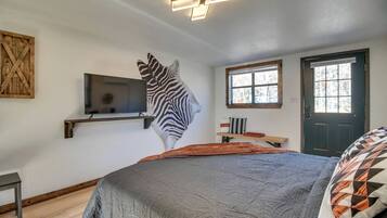 A bedroom with a bed, a mounted TV, a zebra wall art, a window, and a door.