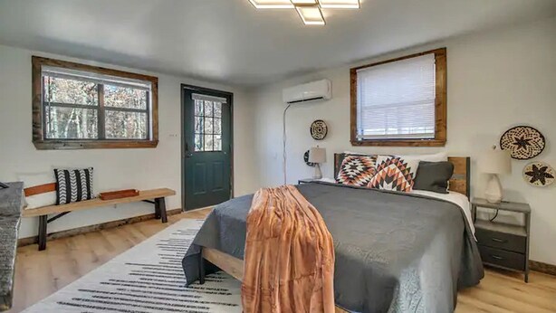 A bedroom with a bed, a bench, a door, and a window.