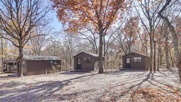 Un terrain de camping comprenant trois cabanes, entouré d’arbres et recouvert de feuilles mortes.