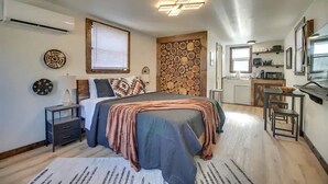 Un dormitorio moderno con cama, mesitas de noche, aire acondicionado instalado en la pared, un área de cocina con microondas y una mesa de comedor.