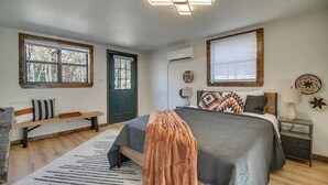 A bedroom with a bed, a bench, a door, and a window. - Serene Woodland Studio Retreat with Outdoor Amenities, Near Fishing, Hiking & Gentry, AR (Gentry)