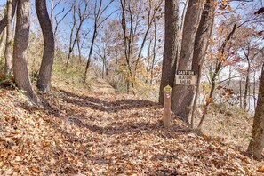 A forest trail with a caution sign indicating a feature ahead. - Serene Woodland Studio Retreat with Outdoor Amenities, Near Fishing, Hiking & Gentry, AR (Gentry)