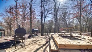 A wooden deck with barbecue grills and a picnic table in a wooded area. - Serene Woodland Studio Retreat with Outdoor Amenities, Near Fishing, Hiking & Gentry, AR (Gentry)