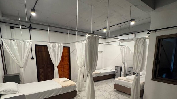 A hotel room with four beds, each with white bedding and curtains, a wooden door, and a marble floor.