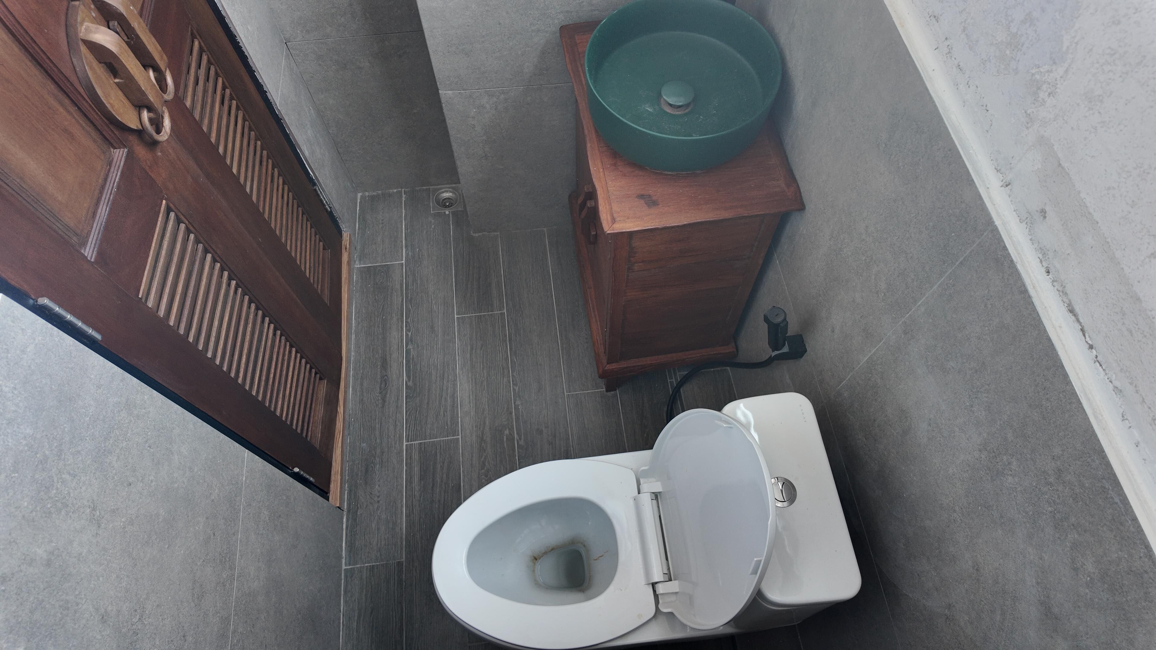 Eine Toilette mit Deckel in Grün, einem Holzkabinett und einer Tür mit Griff.