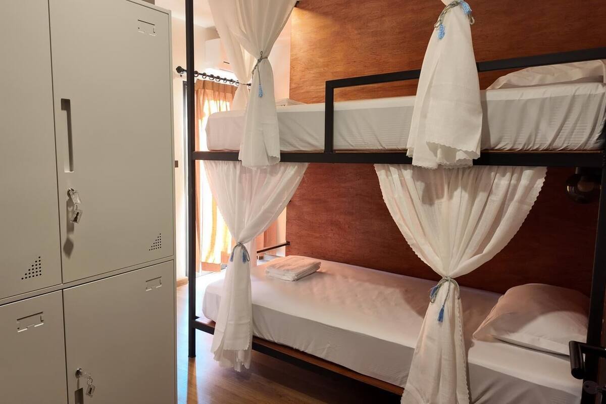 A bunk bed with white bedding and curtains, a wooden headboard, and a metal wardrobe.
