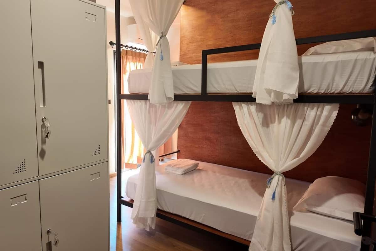 A bunk bed with white bedding and curtains, a wooden headboard, and a metal wardrobe.