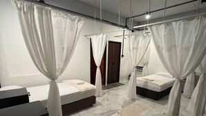 A hotel room with two beds, each with a canopy, a small desk, and a door leading to another room.