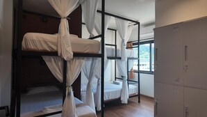 A dormitory room with bunk beds, a wardrobe, and a window with a view.