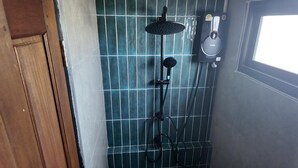 A bathroom with a shower, a handheld showerhead, and a wall-mounted control panel.