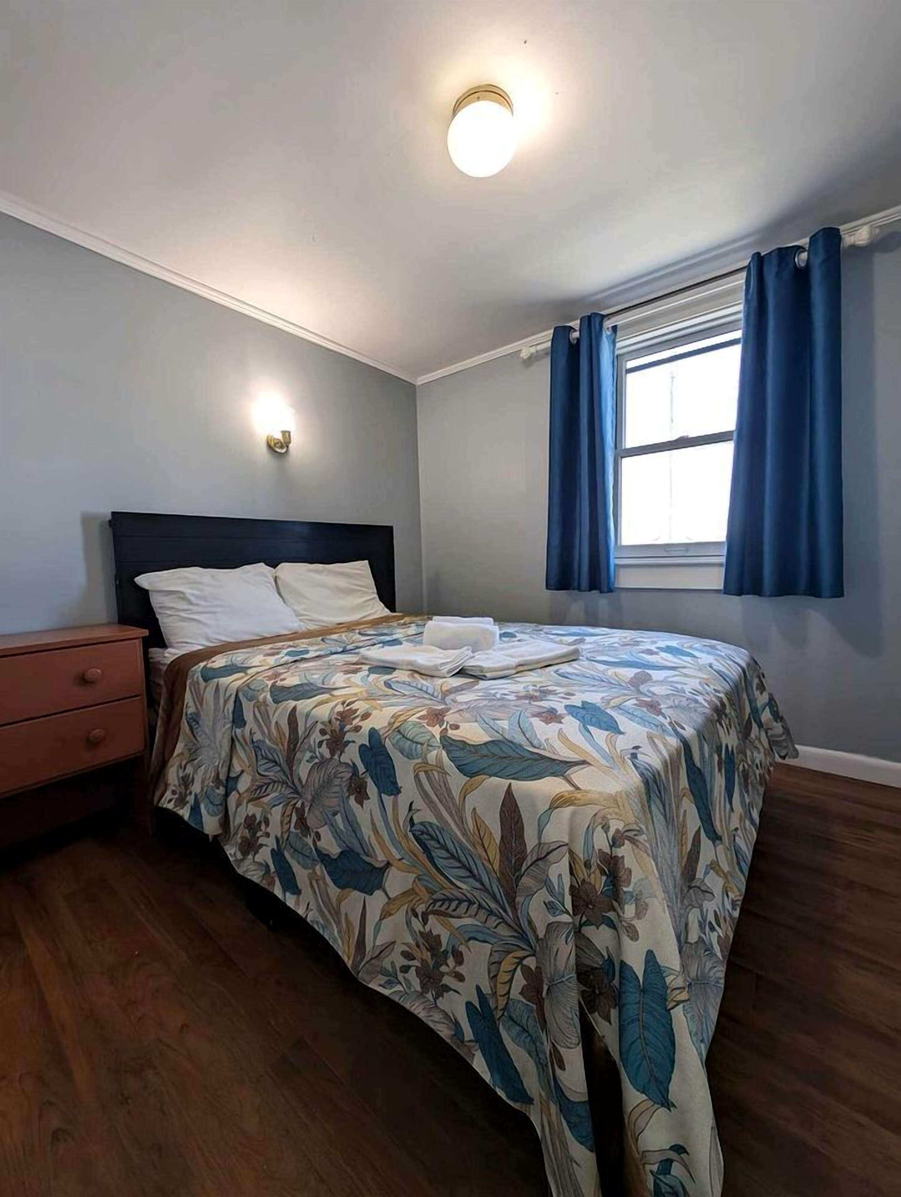 A bedroom with a bed, a nightstand, a window with curtains, and a ceiling light.