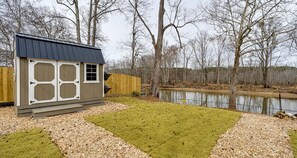 Un petit abri de jardin avec un toit en pente, un espace clôturé avec un étang et une pelouse verdoyante.