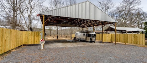 Un espacio al aire libre cubierto con una caravana vintage estacionada bajo una estructura metálica.