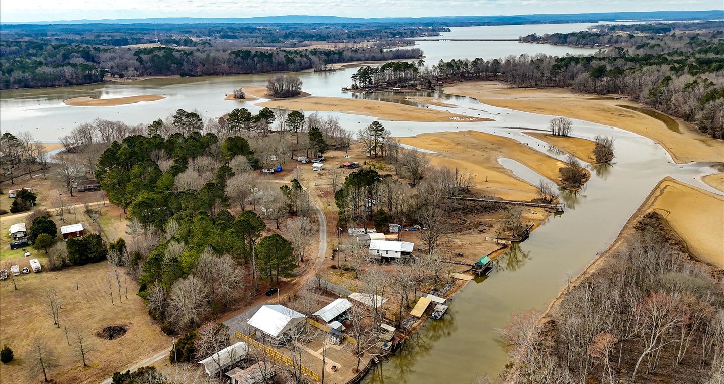 An aerial view of a riverside property with cabins, a dock, and surrounding forested areas.