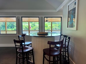 Ein Essbereich mit einem runden Tisch und vier Stühlen, großen Fenstern mit Blick auf Grünflächen und einem gerahmten Bild an der Wand.