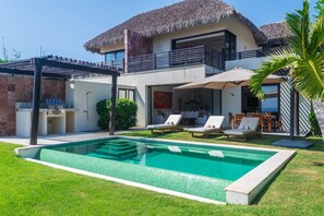 Eine moderne Villa mit Pool, Sitzgelegenheiten im Freien und einem Strohdach.