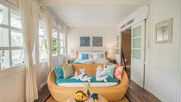 Una habitación con una cama, un sofá de mimbre, una mesa redonda y vistas al exterior.