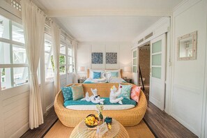 A room with a bed, a wicker sofa, a round coffee table, and a view of the outdoors.