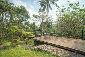 A wooden deck with chairs, surrounded by lush greenery and a palm tree. - Dhamanadi Boutique Resort (Megamendung)