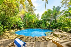 Una piscina rodeada de vegetación tropical, con un muelle de madera y una toalla.