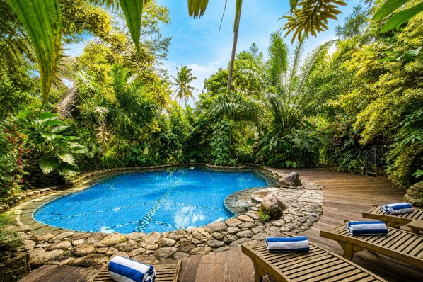 Una piscina circular rodeada por un borde de piedra, con sillas de madera y toallas.