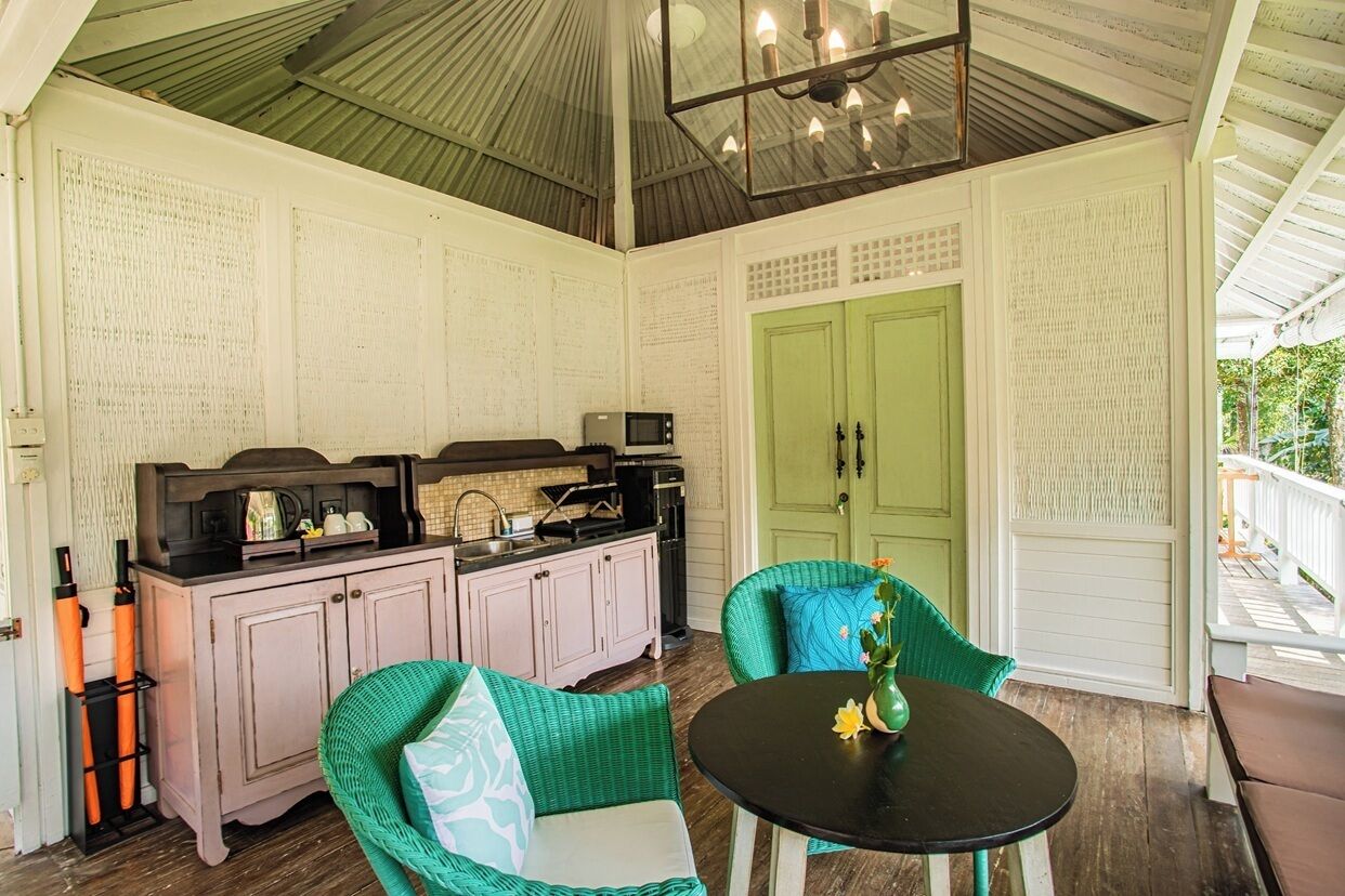Un porche cubierto con una mesa y sillas de comedor, una zona de cocina con armarios y electrodomésticos, y una puerta verde.