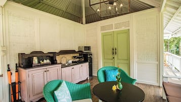 Un porche cubierto con una mesa y sillas de comedor, una zona de cocina con armarios y electrodomésticos, y una puerta verde.