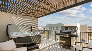 Een balkon met een barbecue, zitplaatsen en uitzicht op gebouwen.