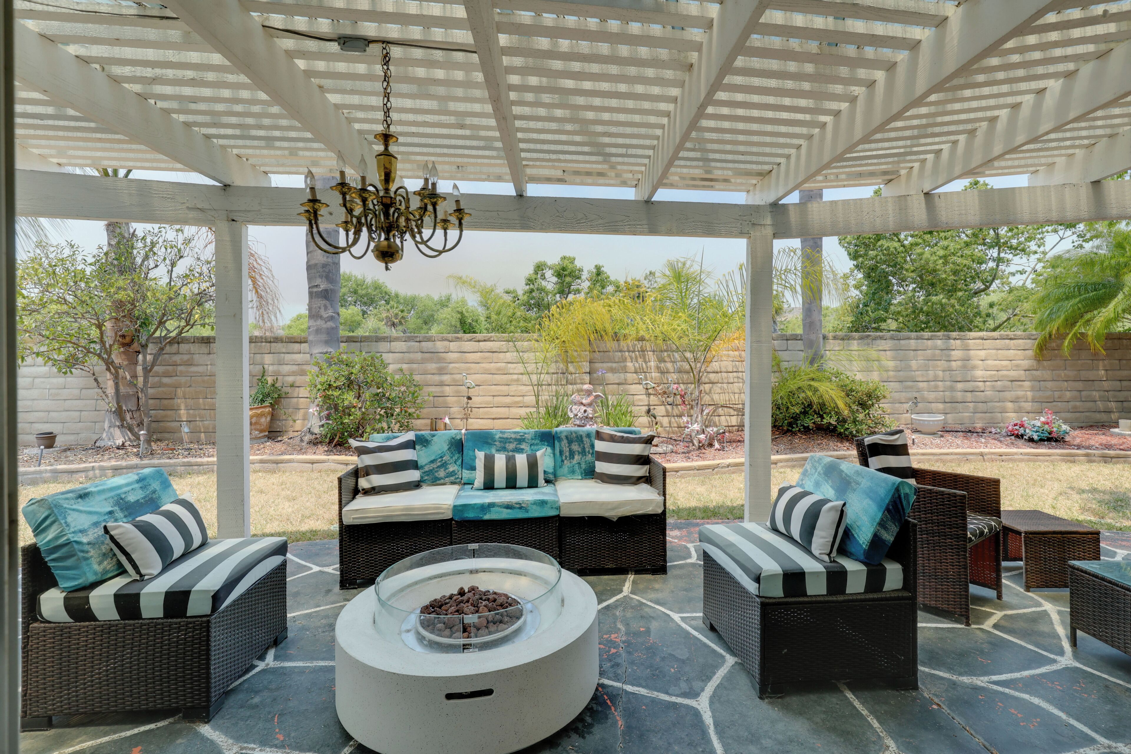 Un espacio al aire libre cubierto con mobiliario de mimbre, un hogar central y una pérgola con candelabro.