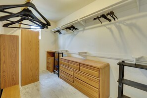 Ein begehbarer Kleiderschrank mit Holzschränken, einem Metallregal und einer weißen Wand mit schwarzen Kleiderbügeln.
