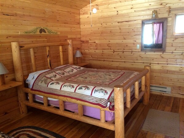 A wooden cabin room with a bed, a wall-mounted mirror, and a small window.