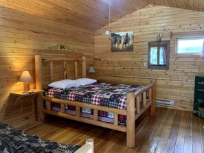 Puinen mökkimainen makuuhuone, jossa on sänky, yöpöytä, lamppu ja taulu seinällä.