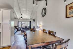 Een ruime eethoek met een grote houten tafel en stoelen, een plafondventilator en een klok aan de muur.