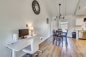 Een moderne keuken met witte kasten, een eettafel met stoelen, een grote klok en een computerinrichting met een lamp.