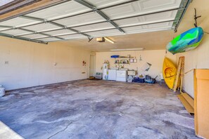 Eine Garage mit Betonboden, einer weißen Tür und verschiedenen Gegenständen, darunter ein gelbes Kajak, ein blaugrünes Objekt und ein weißer Kühlschrank.