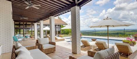 Un espacio exterior techado con mobiliario de mimbre, una piscina y vistas al paisaje.
