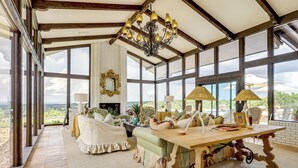 Une pièce spacieuse avec une grande fenêtre, un lustre, une cheminée et une table à manger.
