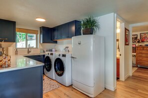 A compact kitchen with a built-in washer and dryer, dark blue cabinets, and a wooden floor. - Private Dock, Deck & Yard: Luxe Sacheen Lake Home (Newport)