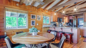 Ein Holzinterieur mit einem runden Esstisch, Barhocker und einer Küchenzeile.