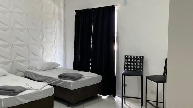 A hotel room with two beds, a window with black curtains, a chair, and an air conditioning unit. - Vista Bela Hotel Pindamonhangaba  (Pindamonhangaba)