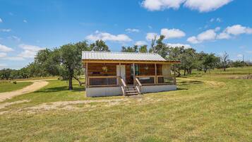 A small wooden cabin with a metal roof, a porch with steps, and a dirt path leading to it.