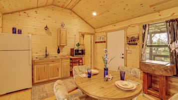 L’intérieur d’un chalet en bois comprend une cuisine, un coin repas et une fenêtre avec des rideaux.