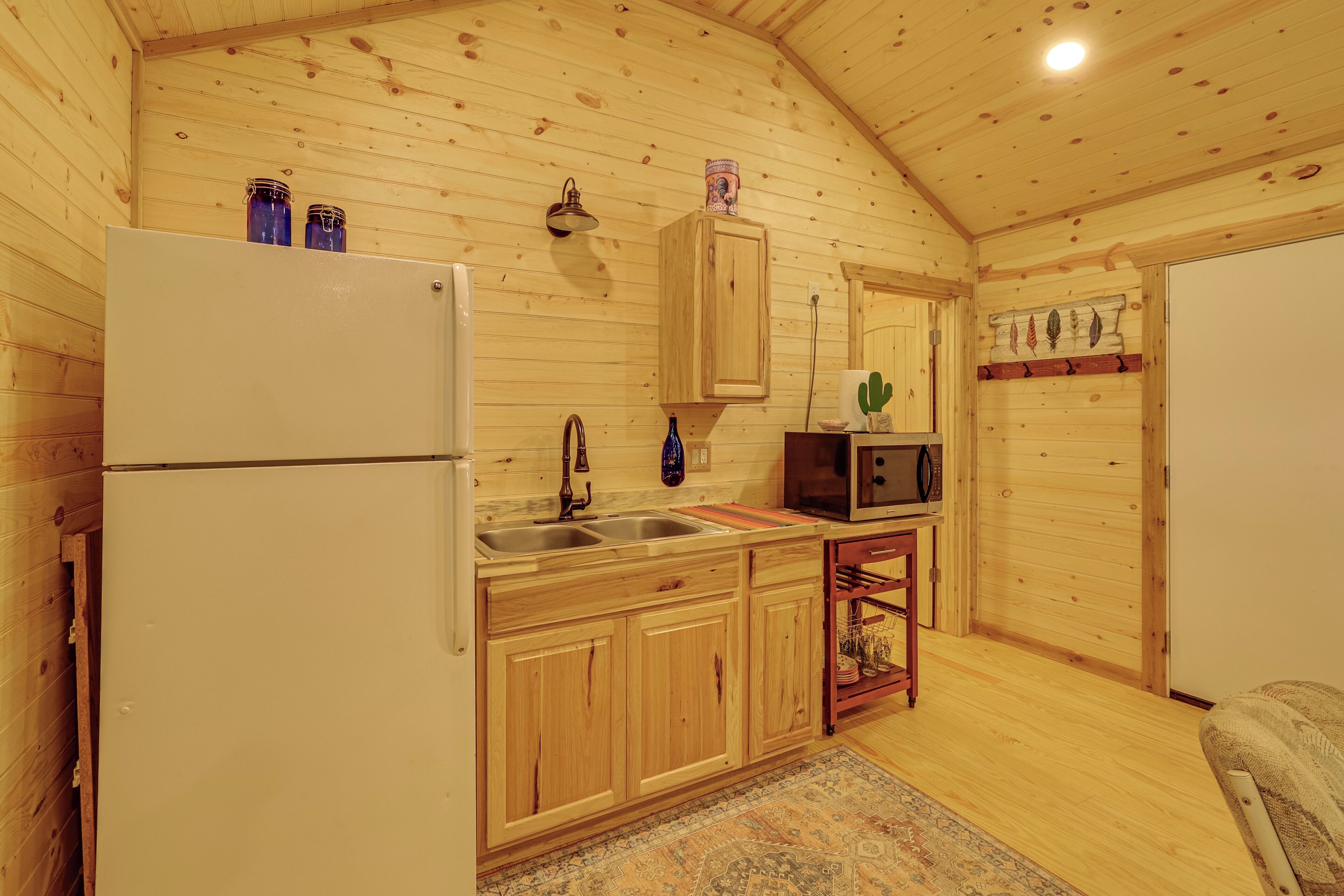 L’intérieur d’un chalet en bois comprend un coin cuisine équipé d’un réfrigérateur, d’un évier, d’un four à micro-ondes et d’armoires en bois.