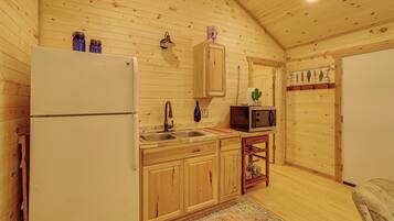L’intérieur d’un chalet en bois comprend un coin cuisine équipé d’un réfrigérateur, d’un évier, d’un four à micro-ondes et d’armoires en bois.