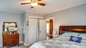 Una camera da letto con un letto, una cassettiera, uno specchio, una ventola a soffitto e una porta che dà su un'altra stanza.