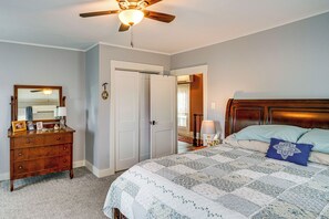 A bedroom with a bed, dresser, mirror, ceiling fan, and a door leading to another room.