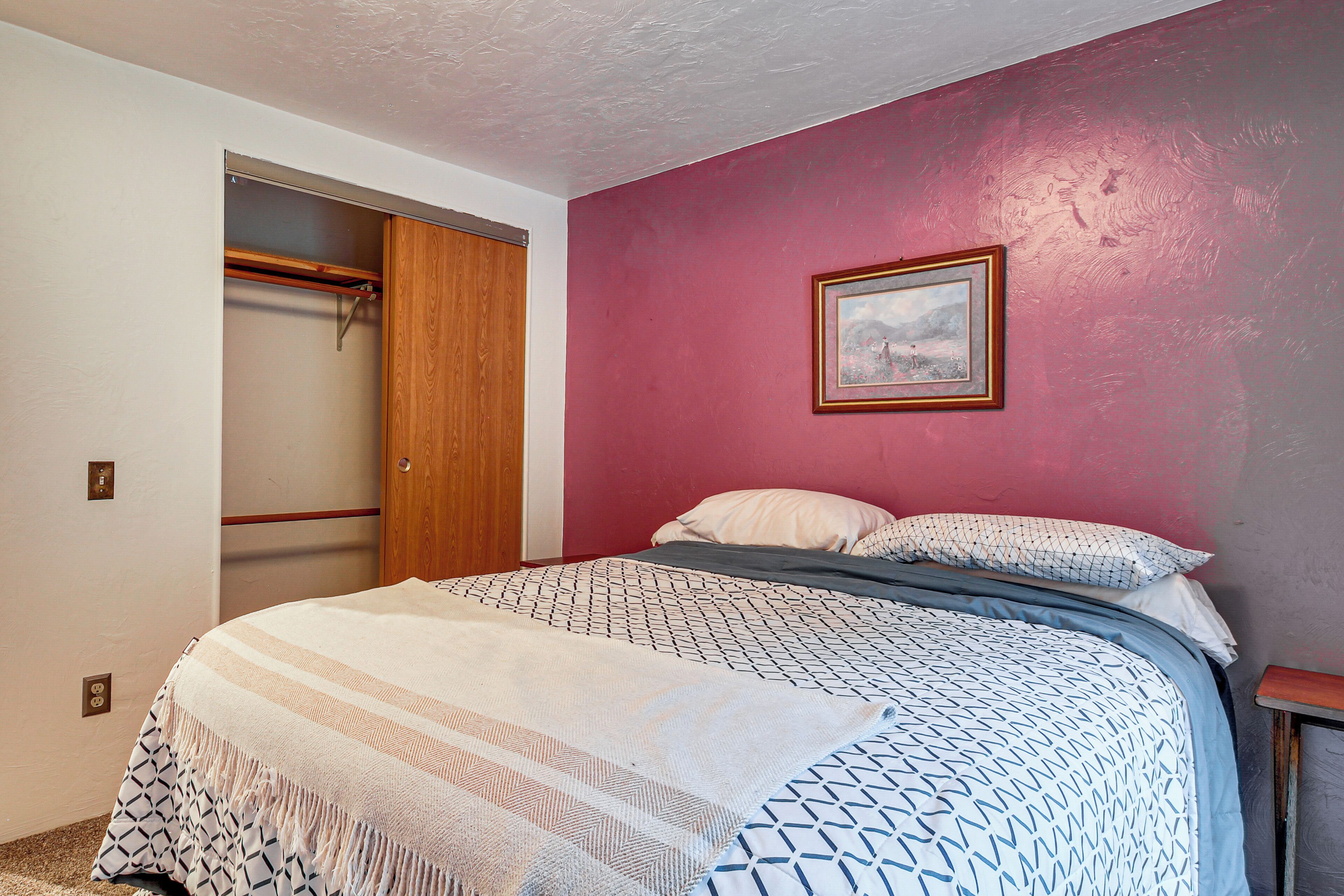 Un dormitorio con cama, armario de madera, cuadro en la pared y pared roja.