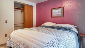 Un dormitorio con cama, armario de madera, cuadro en la pared y pared roja.