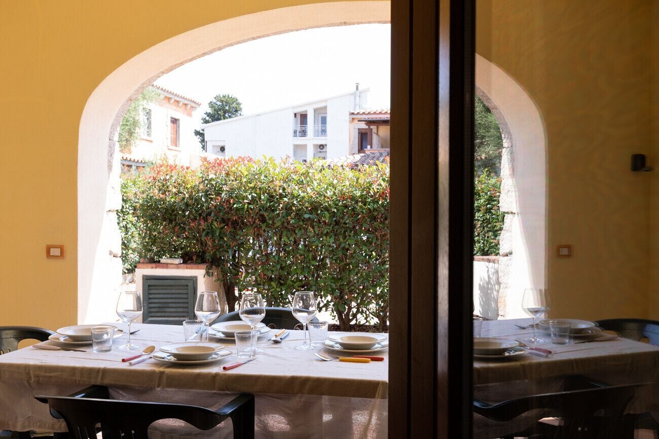 A dining table set with plates, glasses, and cutlery, with an archway leading to a building with balconies.
