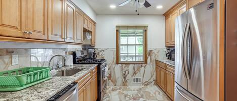 A kitchen with wooden cabinets, a stainless steel refrigerator, a dishwasher, and a window with a view.